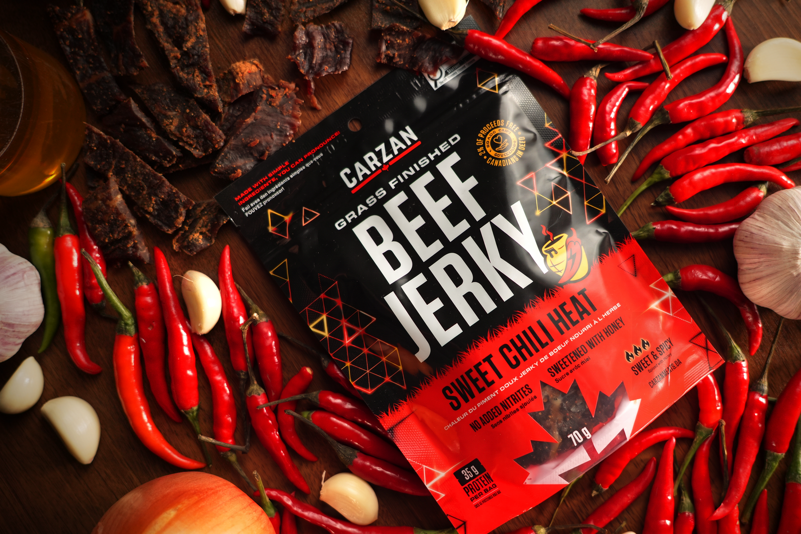 Carzan Sweet Chili Heat beef jerky bag surrounded by chili peppers, garlic, honey, and dried jerky strips